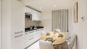 A compact kitchen with white cabinets, a microwave, and a dining area with a round table set for two. - Galea Studio by Wonderful Italy (Genova)
