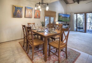 A dining area with a wooden table and chairs, surrounded by artwork and a large window with a scenic view.