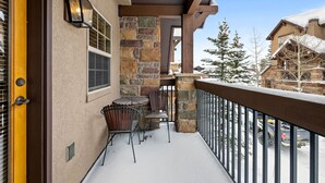 A snow-covered balcony with stone walls, a wooden door, and a view of neighboring buildings. - 3 Miles to Resort | Hot Tub | Fireplace | EV Charger | Great for Groups (Winter Park)