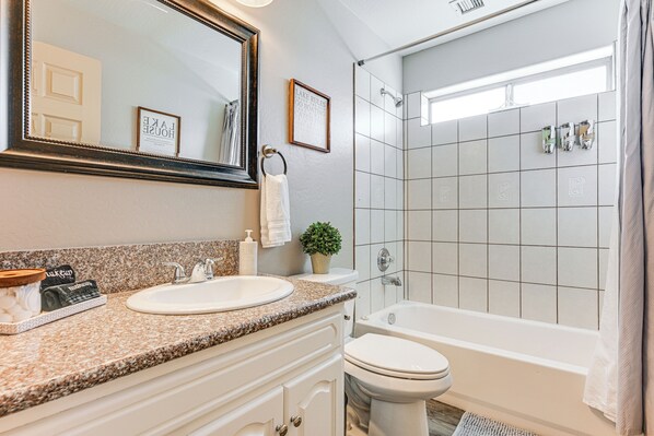 Une salle de bain avec un lavabo, des toilettes et une baignoire. Il y a un miroir au-dessus du lavabo, un porte-serviettes et une citation encadrée accrochée au mur.