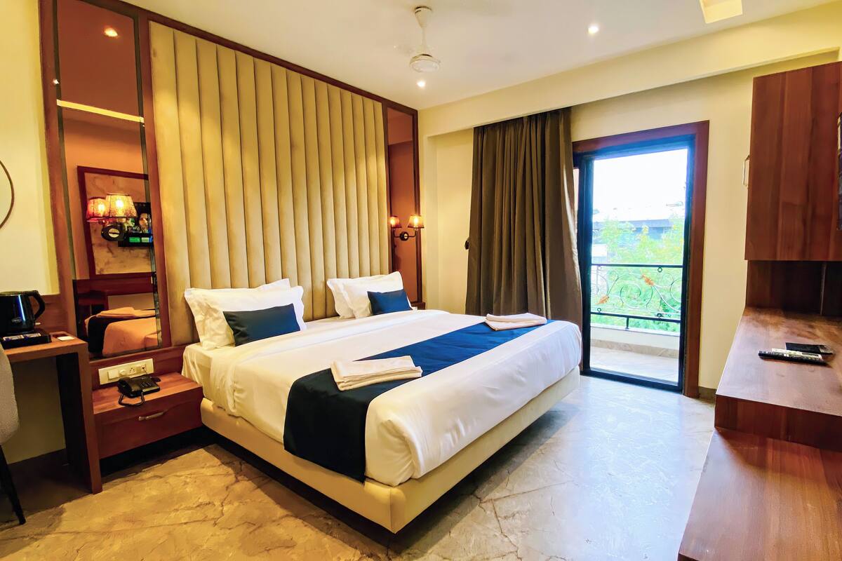 A hotel room with a large bed, a desk with a telephone, a television, and a balcony with a view.