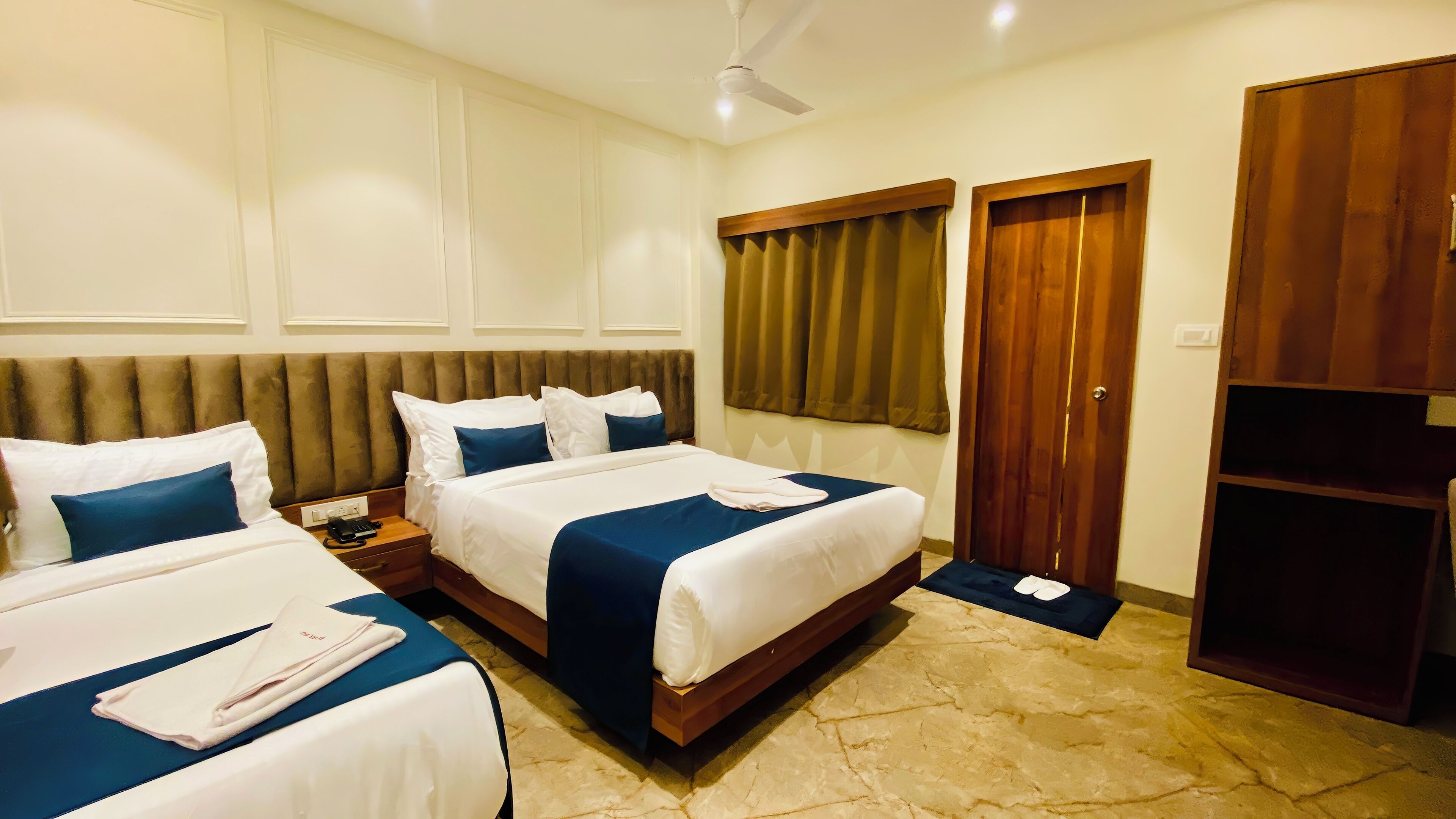 A hotel room with two beds, a wooden headboard, a telephone on the nightstand, and a wardrobe.