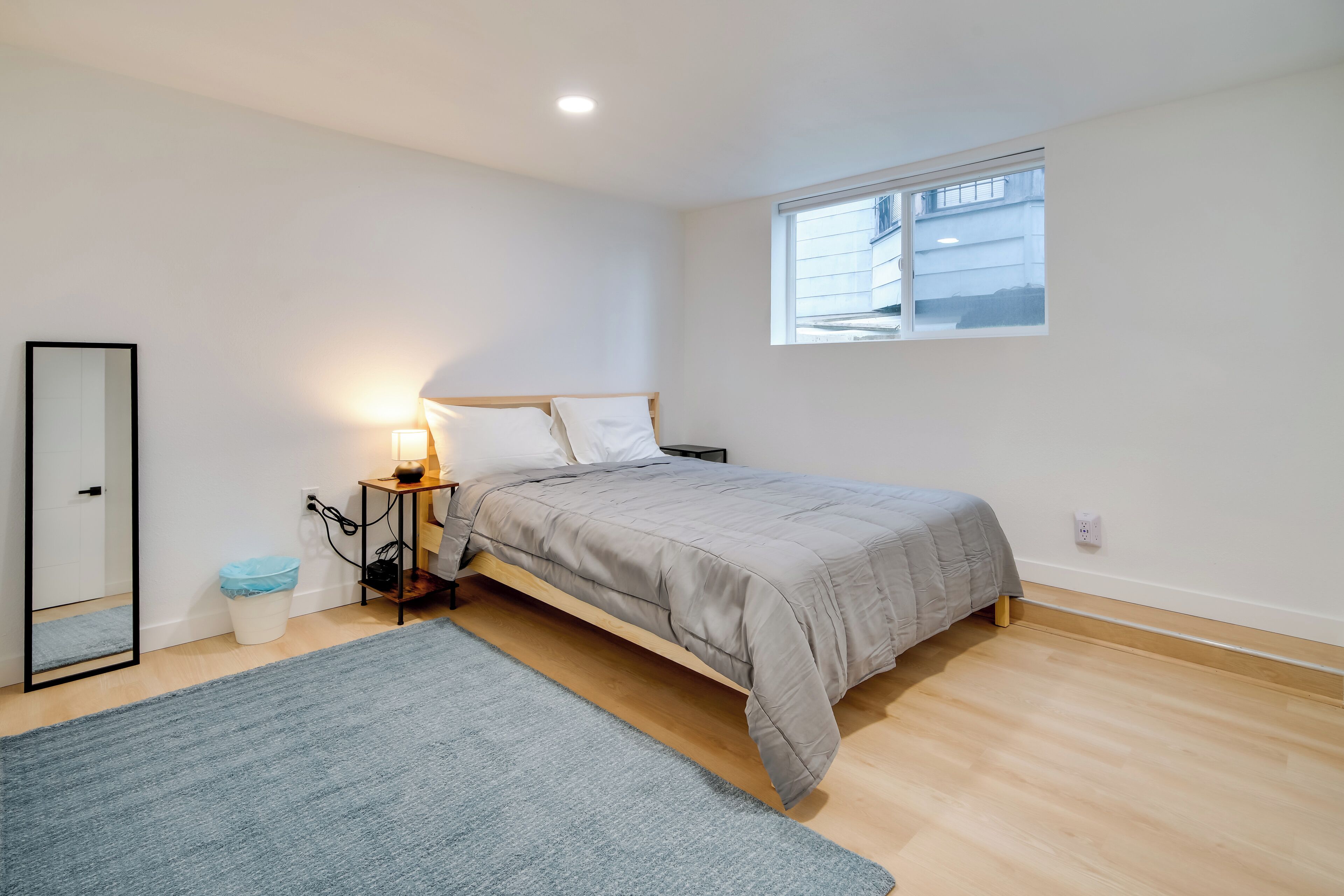 A bedroom with a bed, bedside table, lamp, and a window.