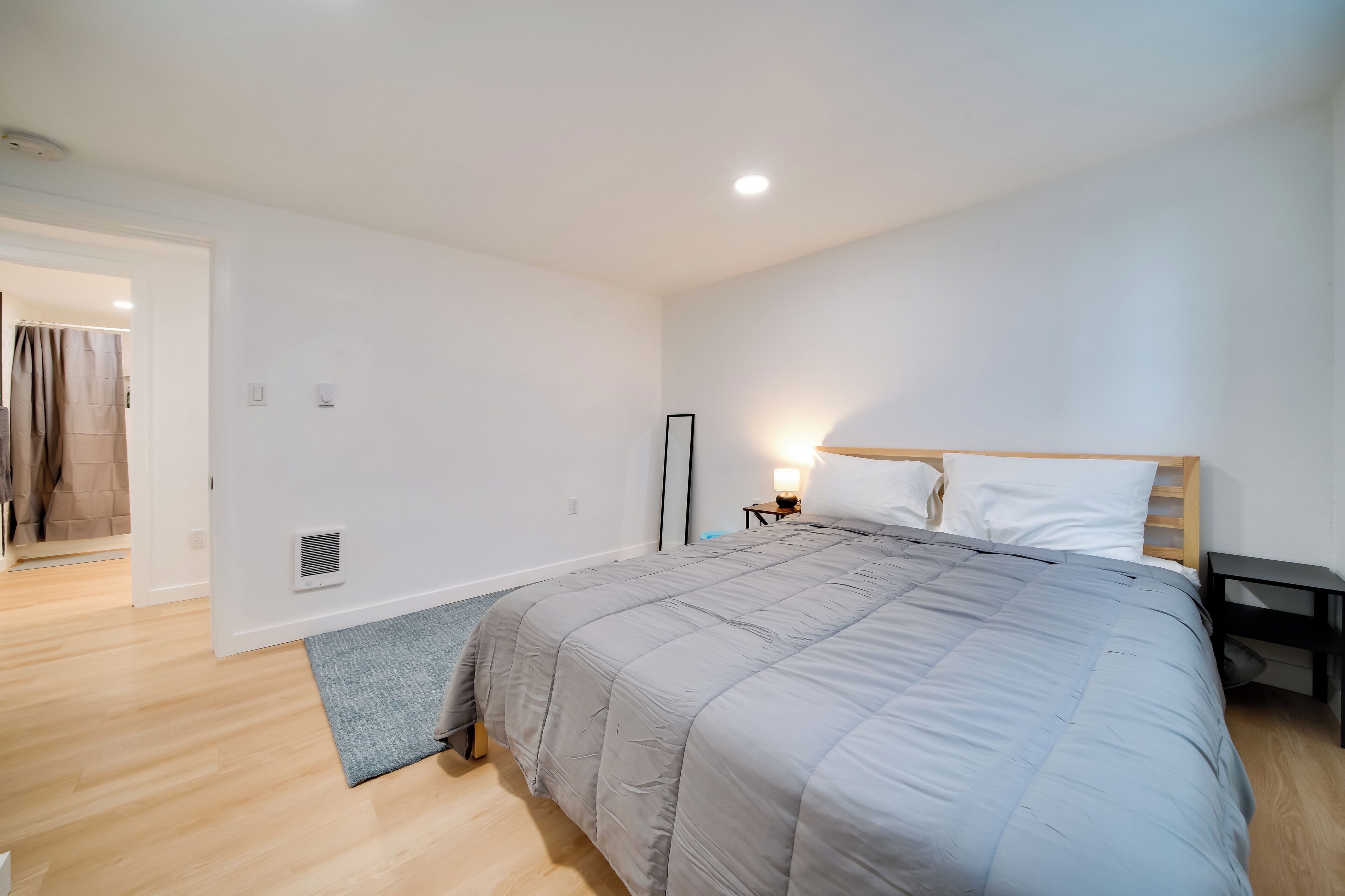 A bedroom with a large bed, a bedside table with a lamp, a wooden headboard, and a door leading to another room.