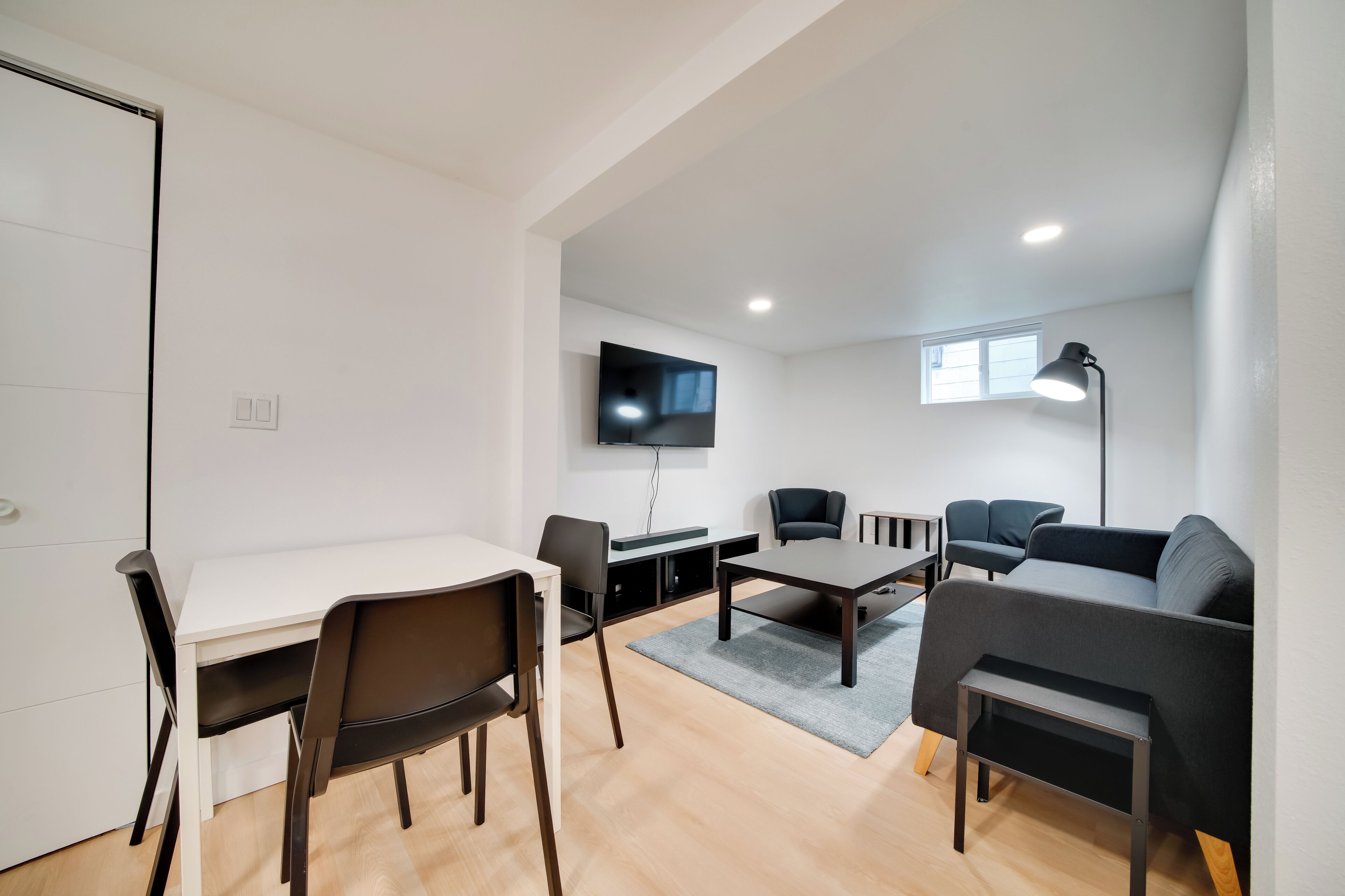 A modern living room with a white table, two chairs, a sofa, a coffee table, and a TV mounted on the wall.