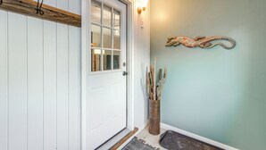 A white door with a glass panel, a wooden shelf above it, a wall-mounted light fixture, and a decorative piece on the wall. - Close to Downtown & Parks: Modern Anchorage Home (Anchorage)