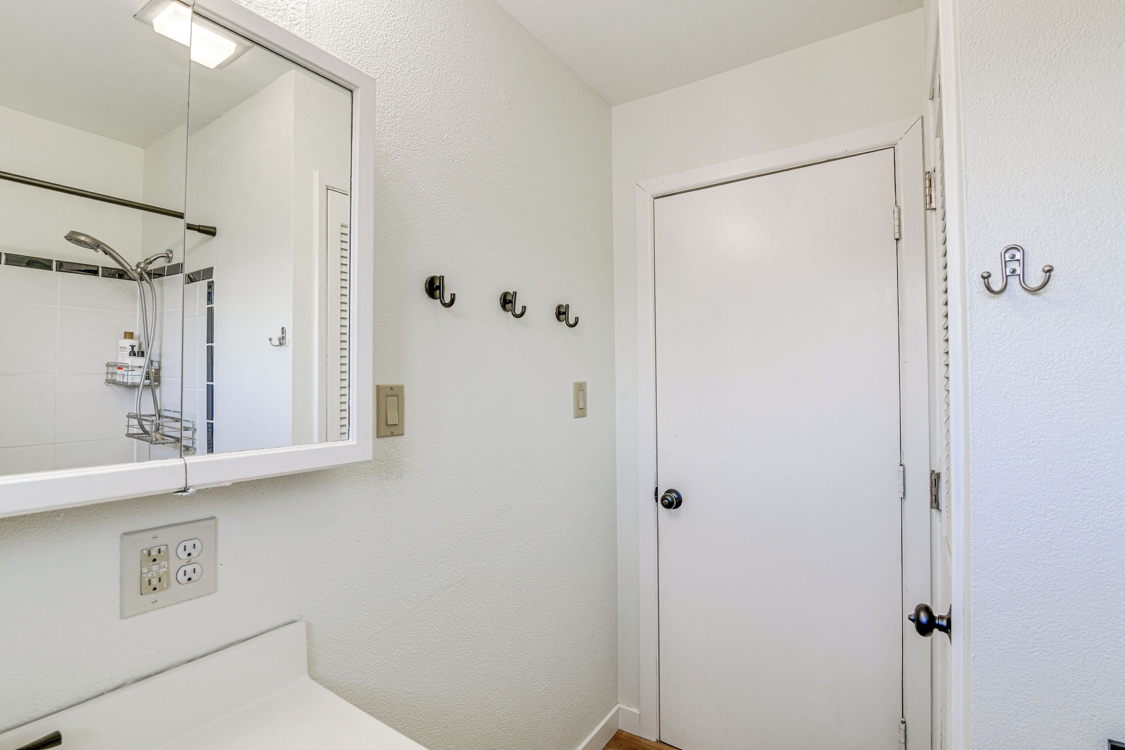 A bathroom with a white sink, a mirror, a shower, and a door with a handle.