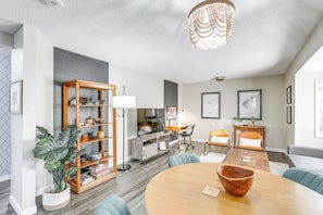 A modern living room with a round wooden table, a bookshelf, a dining area, and a large plant. - Close to Downtown & Parks: Modern Anchorage Home (Anchorage)
