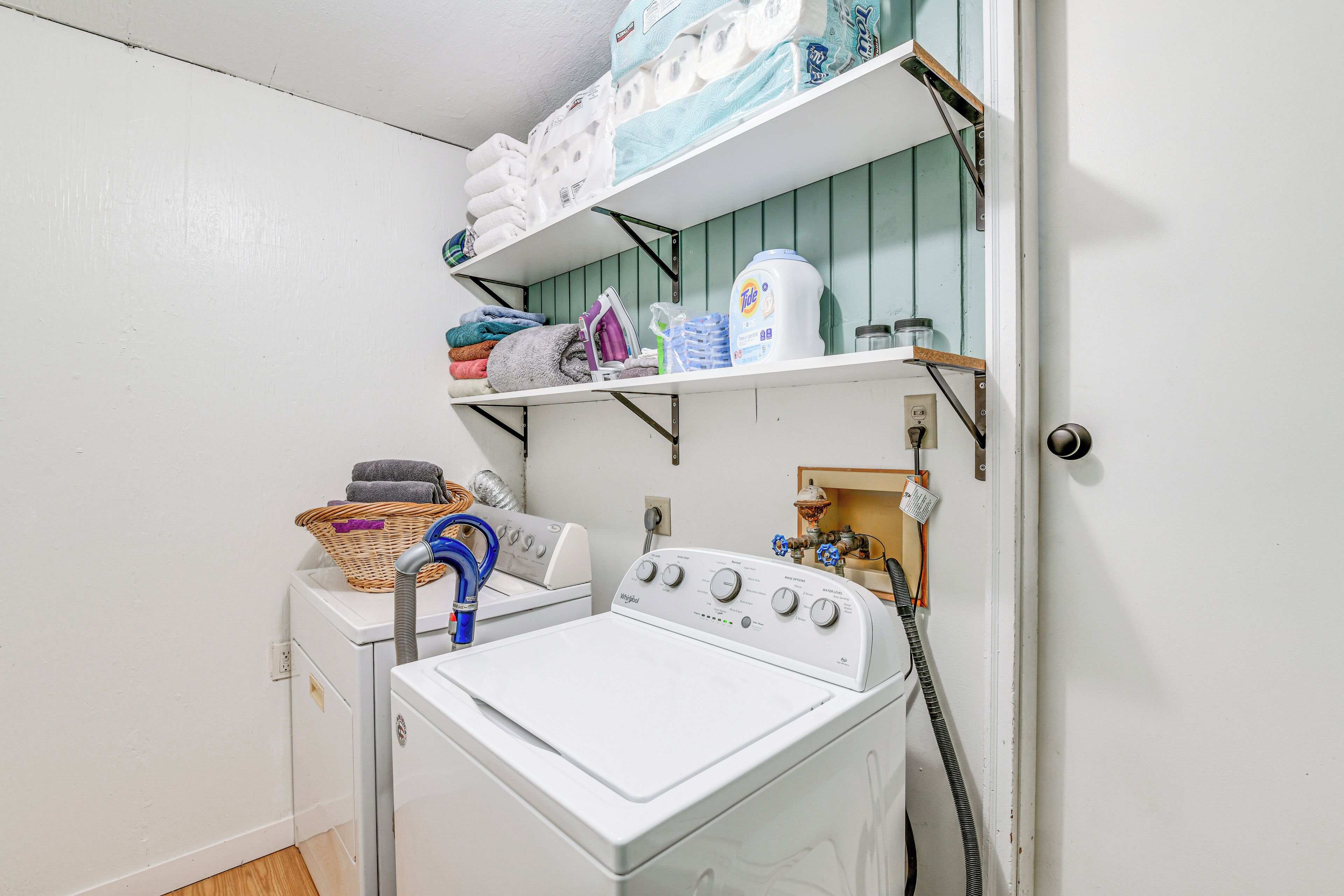 Un espace buanderie comprenant un lave-linge, un sèche-linge, des étagères avec des serviettes pliées et des produits de lessive.