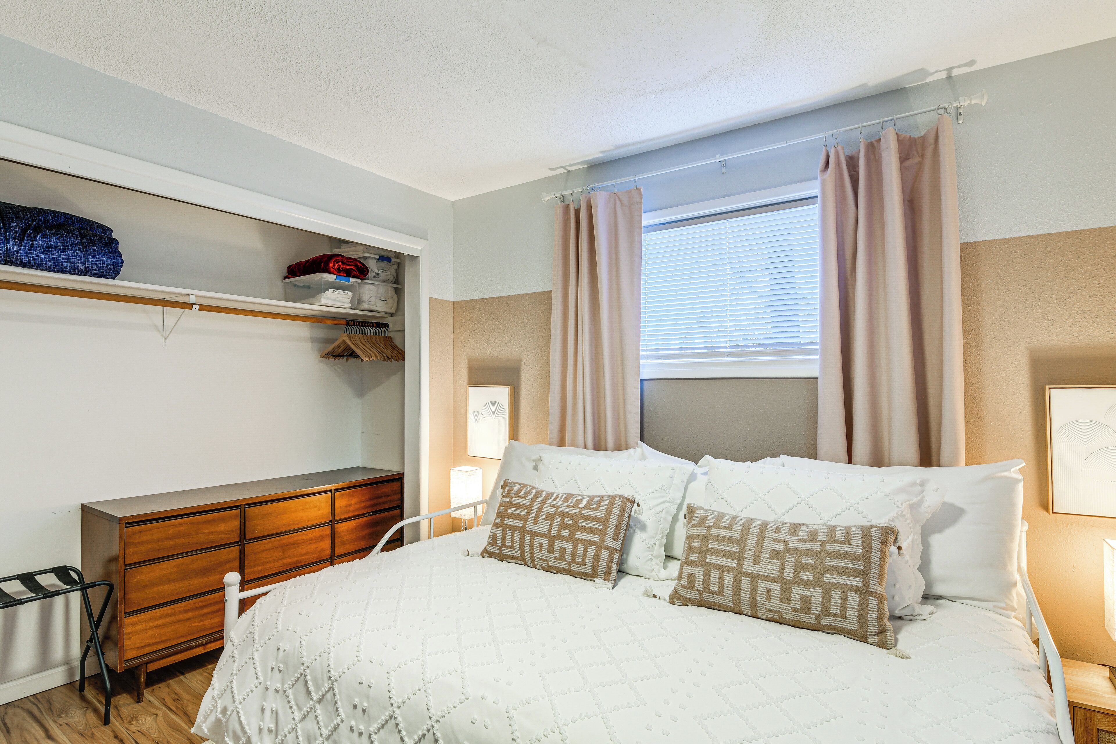 Un dormitorio con cama, cómoda, armario y ventana con cortinas.