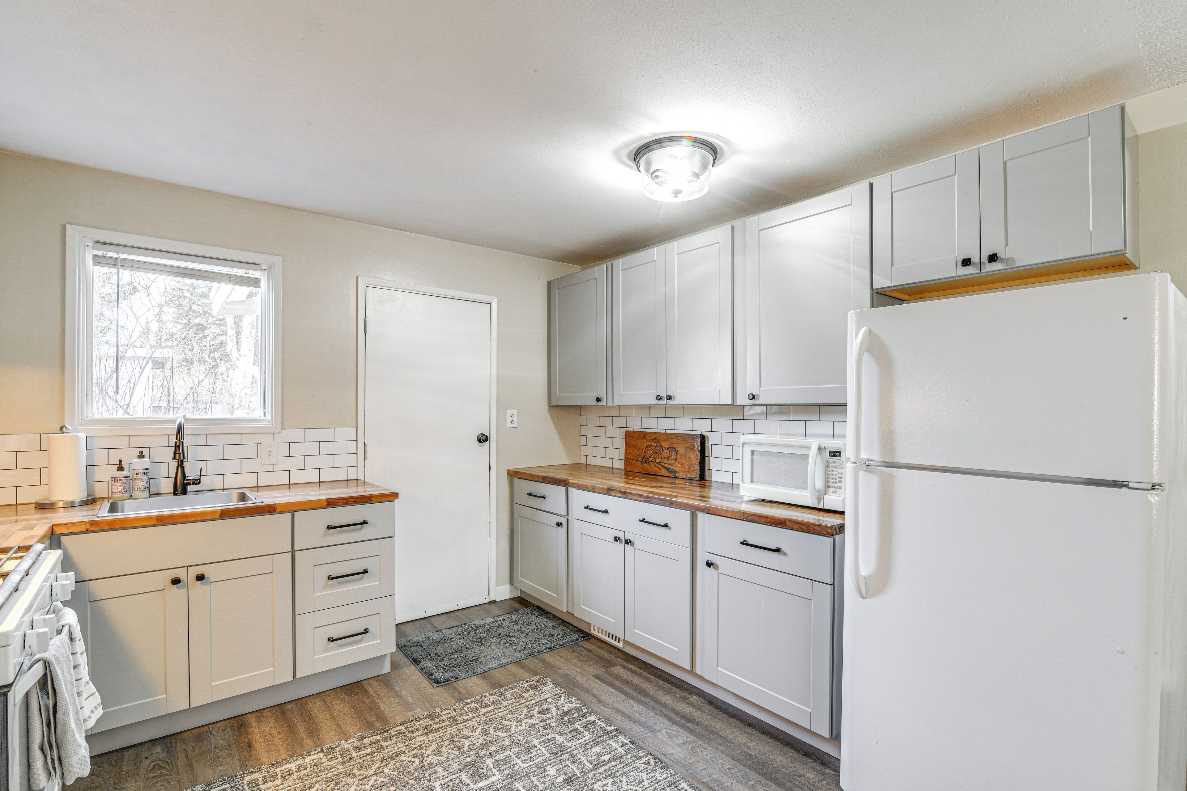 A kitchen with white cabinets, a wooden countertop, a refrigerator, and a window with blinds.