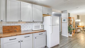 A kitchen with white cabinets, a microwave, and a refrigerator. There is a wooden countertop and a plant in the corner. - Close to Downtown & Parks: Modern Anchorage Home (Anchorage)