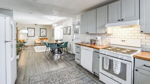 A modern kitchen with grey cabinets, a white stove, and a dining area with a table and chairs. - Close to Downtown & Parks: Modern Anchorage Home (Anchorage)