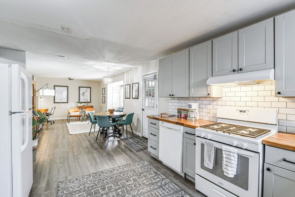 A modern kitchen with grey cabinets, a white stove, and a dining area with a table and chairs. - Close to Downtown & Parks: Modern Anchorage Home (Anchorage)