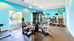 Un gimnasio con diversas máquinas de ejercicio, un ventanal grande y un ventilador de techo.