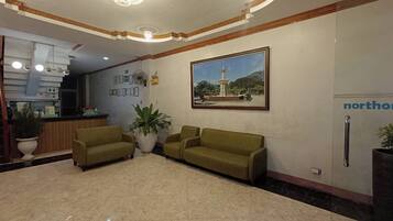 A lobby with a reception desk, two sofas, a large potted plant, and a framed picture of a fountain.