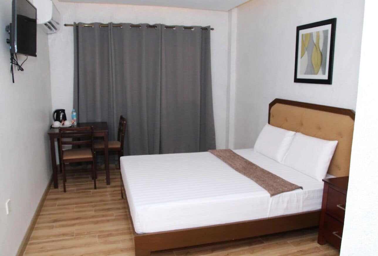Ein Hotelzimmer mit Bett, Schreibtisch mit Stühlen, Fernseher und einem gerahmten Bild an der Wand.