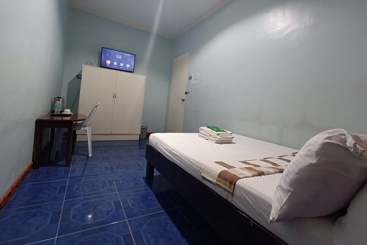 A small, clean room with a bed, a desk, a cabinet, and a television on the wall.
