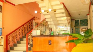 A reception area with a staircase, a reception desk, and a large plant. - Northomes Pensione by HiveRooms (Bogo)