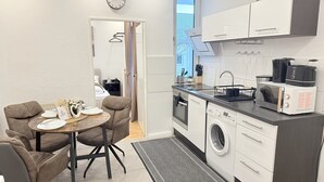 A compact kitchen with a washing machine, microwave, and toaster. There is a dining area with a table and chairs. - Apartment Bremen Neustadt (Bremen)
