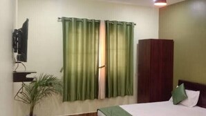 Une chambre à coucher avec un lit, des rideaux verts, une armoire en bois, une plante en pot et un luminaire au plafond.