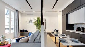 A modern living room with a grey sofa, a dining table set for four, and a kitchen area with dark cabinets and a marble countertop. - Superb apartment with AC - Center of Paris (Paris)