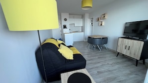 A modern living room with a black and yellow sofa, a small wooden table, a TV, and a kitchen in the background. - PLEINE MER Front de Mer - 1st Et. Elevator - 4P - Parking - Wifi - Linen Ok (Courseulles-sur-Mer)