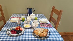 A breakfast table with a checkered tablecloth, plates, bowls, a pitcher, and a plate of croissants and fruit. - Henllys Estate B&B (Llandovery)