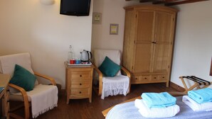 A cozy room with a wooden cabinet, a television mounted on the wall, a small table with a kettle, and a chair with a green pillow. - Henllys Estate B&B (Llandovery)