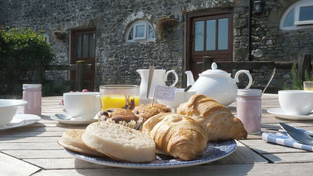 A breakfast setting with croissants, muffins, and a jug of orange juice on a table outside a stone building with windows. - Henllys Estate B&B (Llandovery)