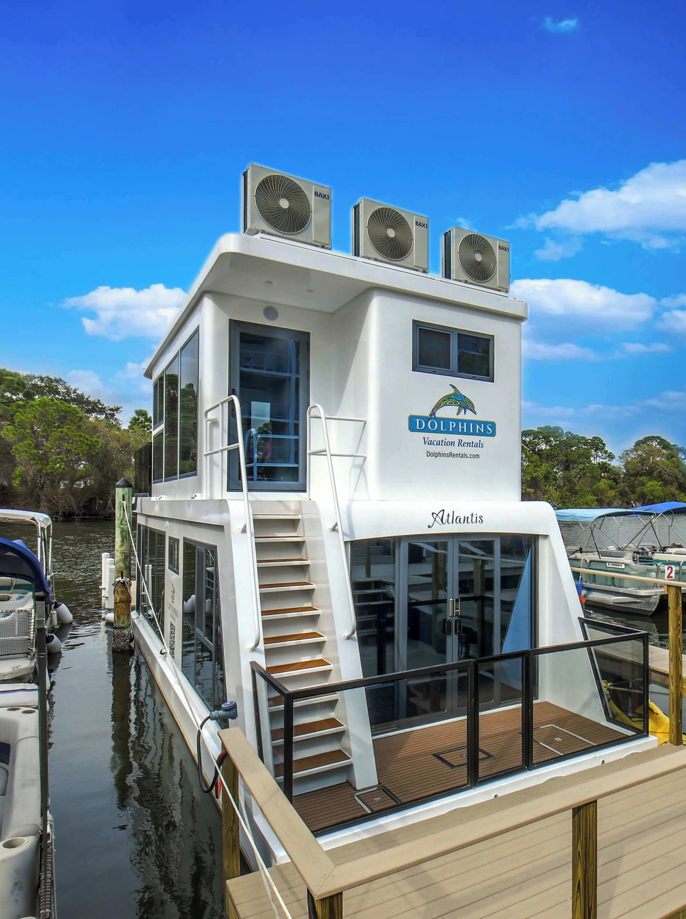 A white boat with a balcony, a logo for Dolphins Vacation Rentals, and the name 'Atlantis' on the side.