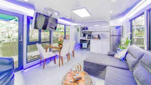 A modern living area with a sofa, dining table, and kitchen in the background. - Avalon 2-Bedroom Floating Home (Merritt Island)