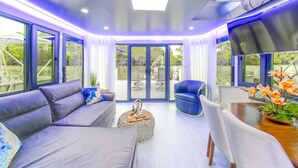 A modern interior with a sofa, armchair, dining table, and large windows. - Avalon 2-Bedroom Floating Home (Merritt Island)