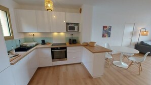 Una cocina moderna con armarios blancos, microondas, lavaplatos y un comedor con mesa y sillas blancas.
