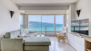 Un salon moderne avec un canapé, un fauteuil, un téléviseur et une grande fenêtre donnant sur la mer.