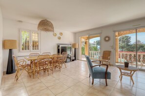 Un vaste espace de vie comprenant un coin repas avec une table et des chaises, un téléviseur et un balcon offrant une vue sur la mer.