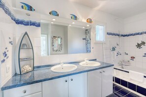 Une salle de bain avec deux lavabos, un grand miroir et des carreaux décoratifs représentant des poissons.