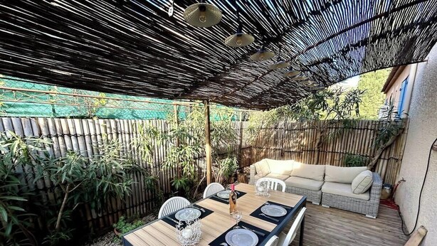 An outdoor patio with a wooden table set for four, surrounded by white chairs.