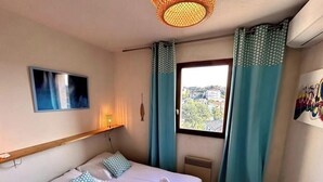 A hotel room with a bed, two pillows, a window with curtains, a wall-mounted TV, and a heater.