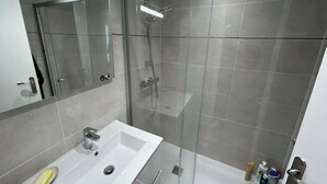 A modern bathroom with a glass-enclosed shower, a white sink, and a mirror above it. - Spacious and fully equipped apartment (Bormes-les-Mimosas)