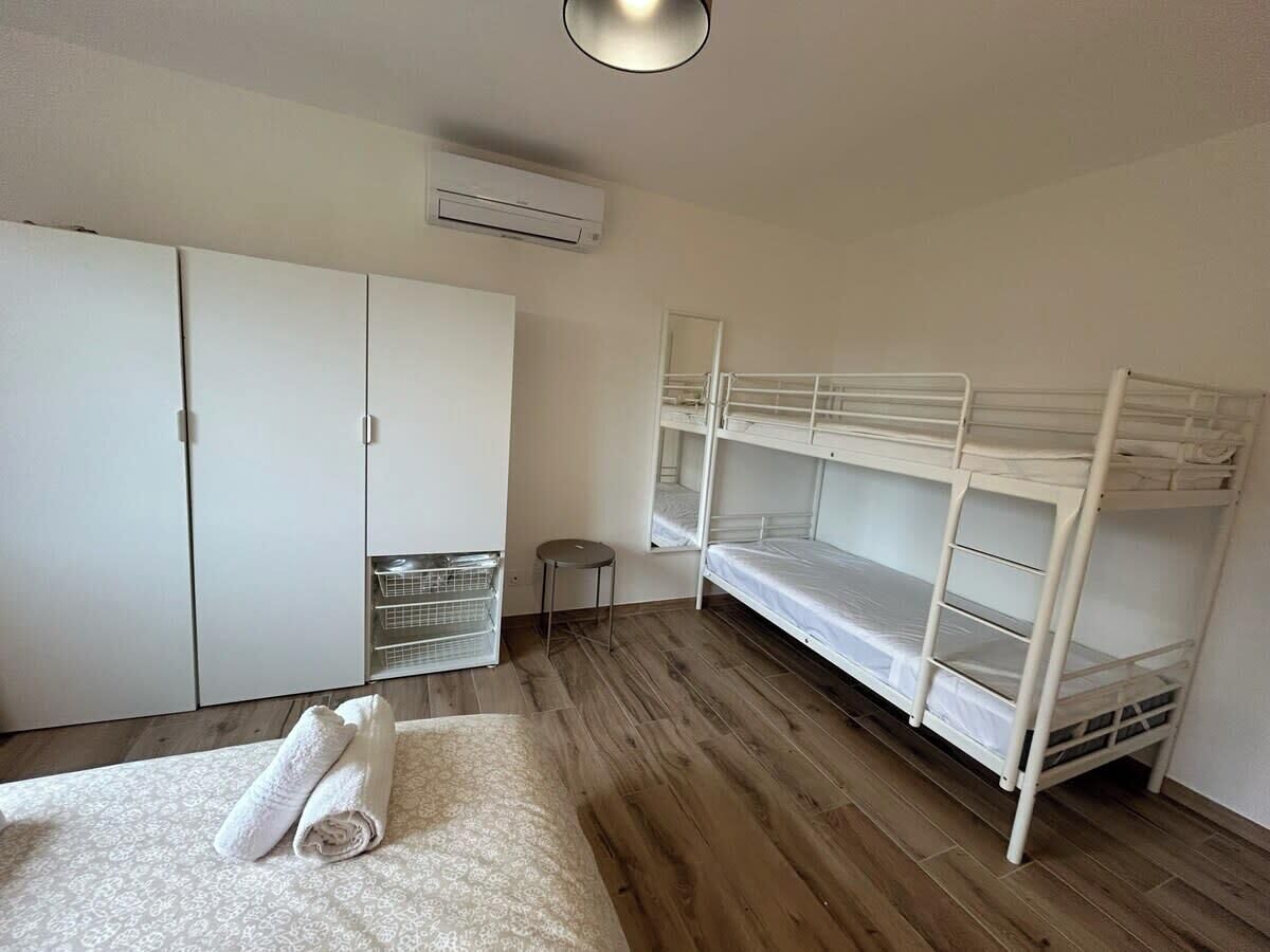 A bedroom with a bunk bed, a wardrobe, a small stool, and a rolled-up towel on the floor.