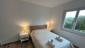 A bedroom with a bed, two bedside tables with lamps, a window with a view, and wooden flooring. - Spacious and fully equipped apartment (Bormes-les-Mimosas)