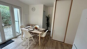 A dining area with a table set for four, white chairs, a clock on the wall, and a sliding door leading outside. - Spacious and fully equipped apartment (Bormes-les-Mimosas)