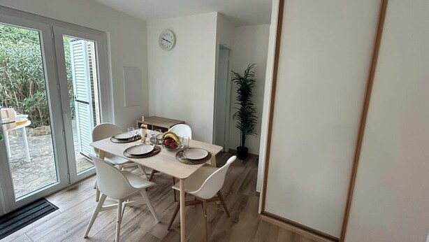 A dining area with a table set for four, white chairs, a clock on the wall, and a potted plant. - Spacious and fully equipped apartment (Bormes-les-Mimosas)