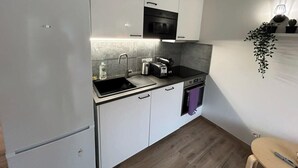 A compact kitchen with white cabinets, a black countertop, a built-in oven, and a microwave. - Spacious and fully equipped apartment (Bormes-les-Mimosas)