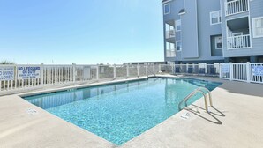 A swimming pool with a white fence and signs stating no lifeguard on duty.