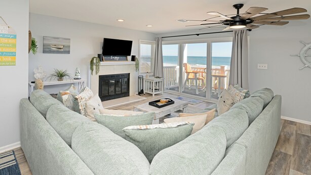 A living room with a large green sofa, a fireplace, a television, and a view of the ocean through large sliding doors.