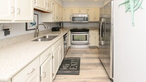 A kitchen with white cabinets, stainless steel appliances, and a black doormat with "Let's EAT" written on it.