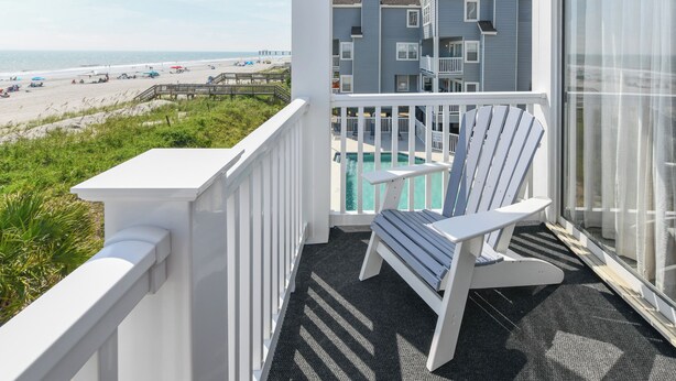 Een balkon met uitzicht op het strand, een zwembad en een gebouw op de achtergrond.
