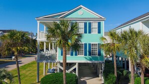 A two-story house with a balcony, surrounded by palm trees and a well-maintained lawn. - 2nd Row 4 BR Beach House with a Shared Pool! - Chubby's Anchor (Surfside Beach)